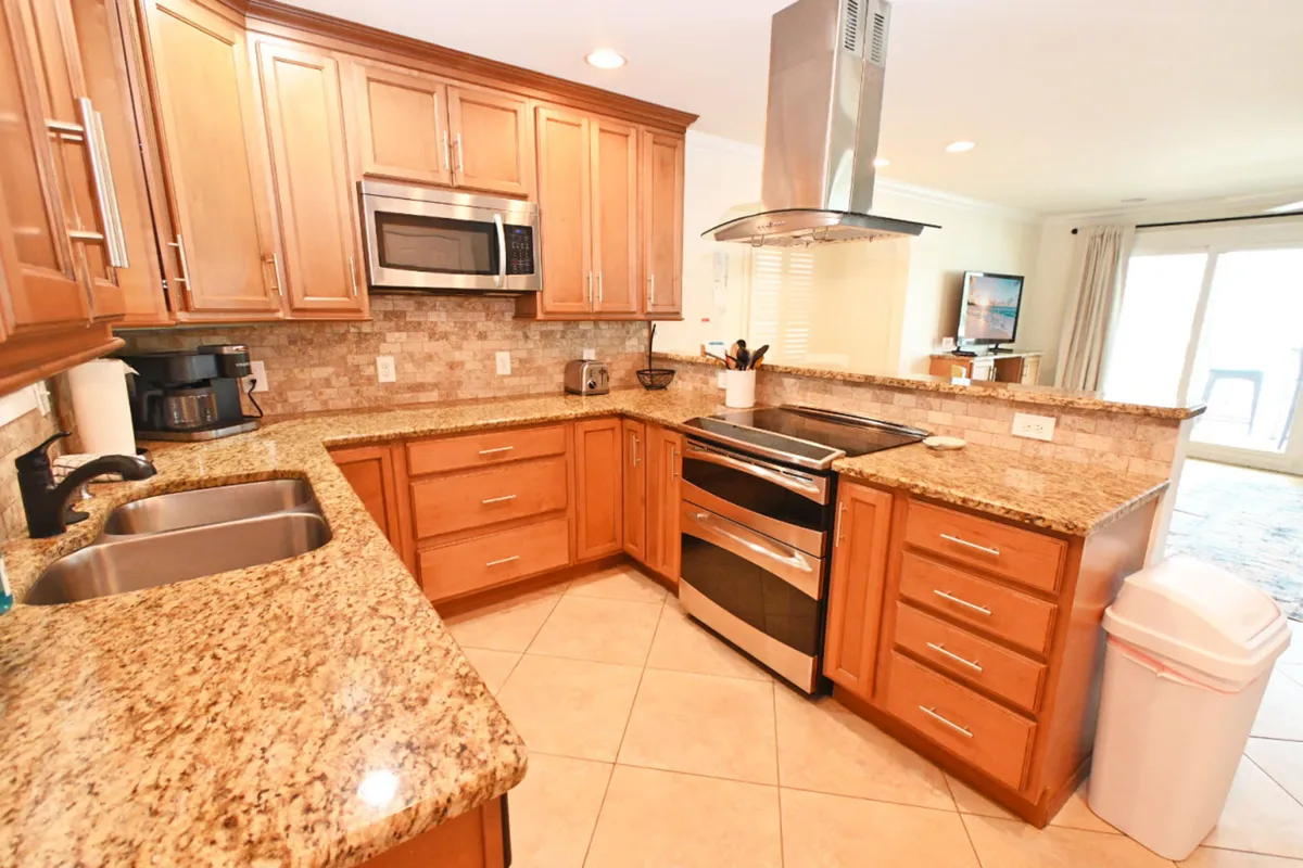 An inviting, fully equipped kitchen with granite countertops, stainless steel appliances, wooden cabinetry, and a double sink. The space is designed for preparing meals and socializing, with the kitchen counter acting as a gathering spot.
