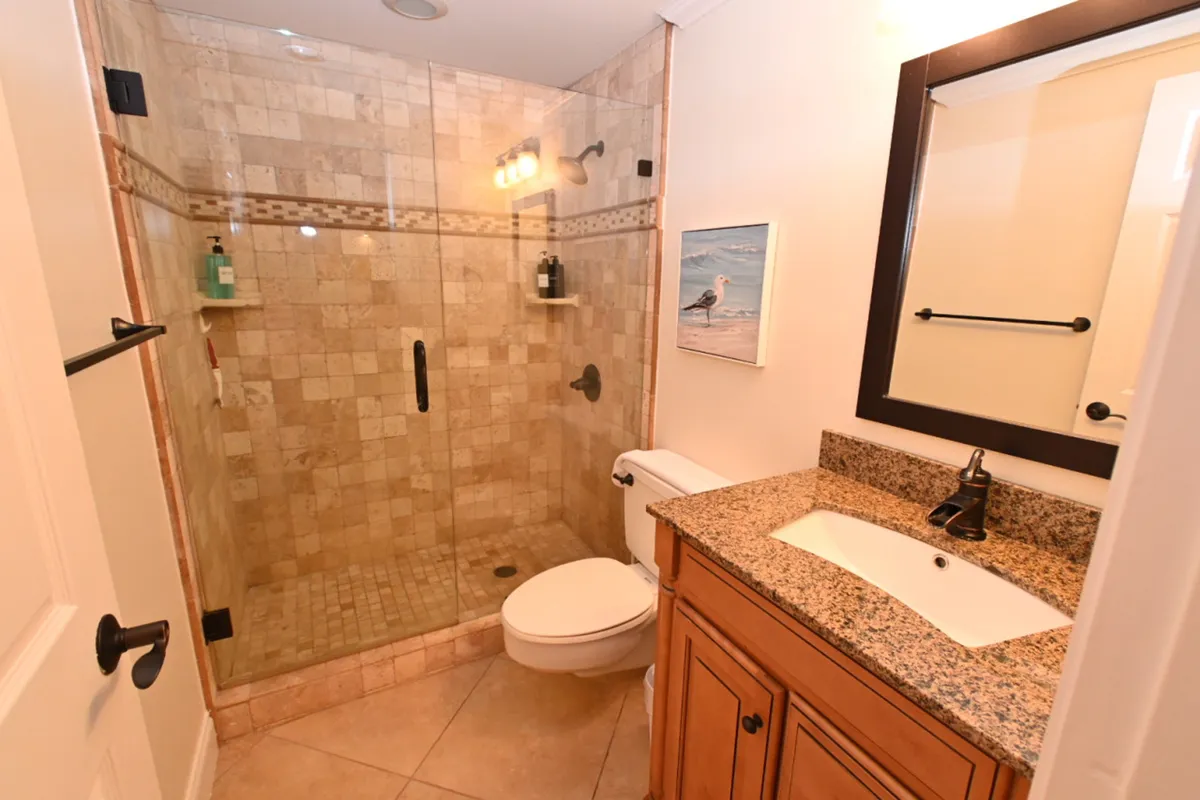 A stylish bathroom with a glass-enclosed tiled shower, granite countertop vanity, toilet, and decorative wall art. The setting is clean, modern, and inviting, offering a spa-like atmosphere for daily routines.