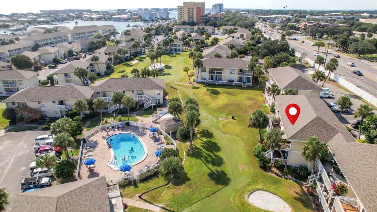 A lively exterior scene featuring a heated community pool surrounded by lounge chairs and umbrellas, a well-kept green golf putting area with a sand trap, and the resort’s condominium buildings in the background. The setting shows both aquatic and land-based amenities, ideal for families seeking diverse activities.