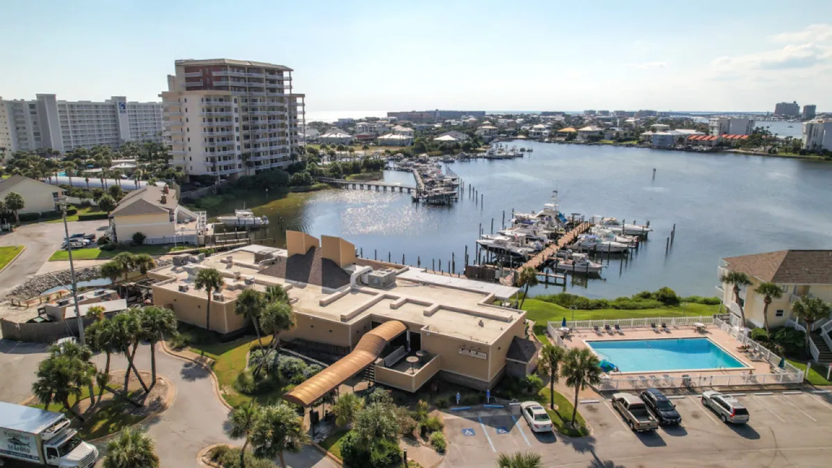 A marina with docked boats, a large swimming pool, resort buildings, and a waterway leading to the open gulf. The scene is relaxed yet vibrant, highlighting boating, swimming, and easy Gulf access.